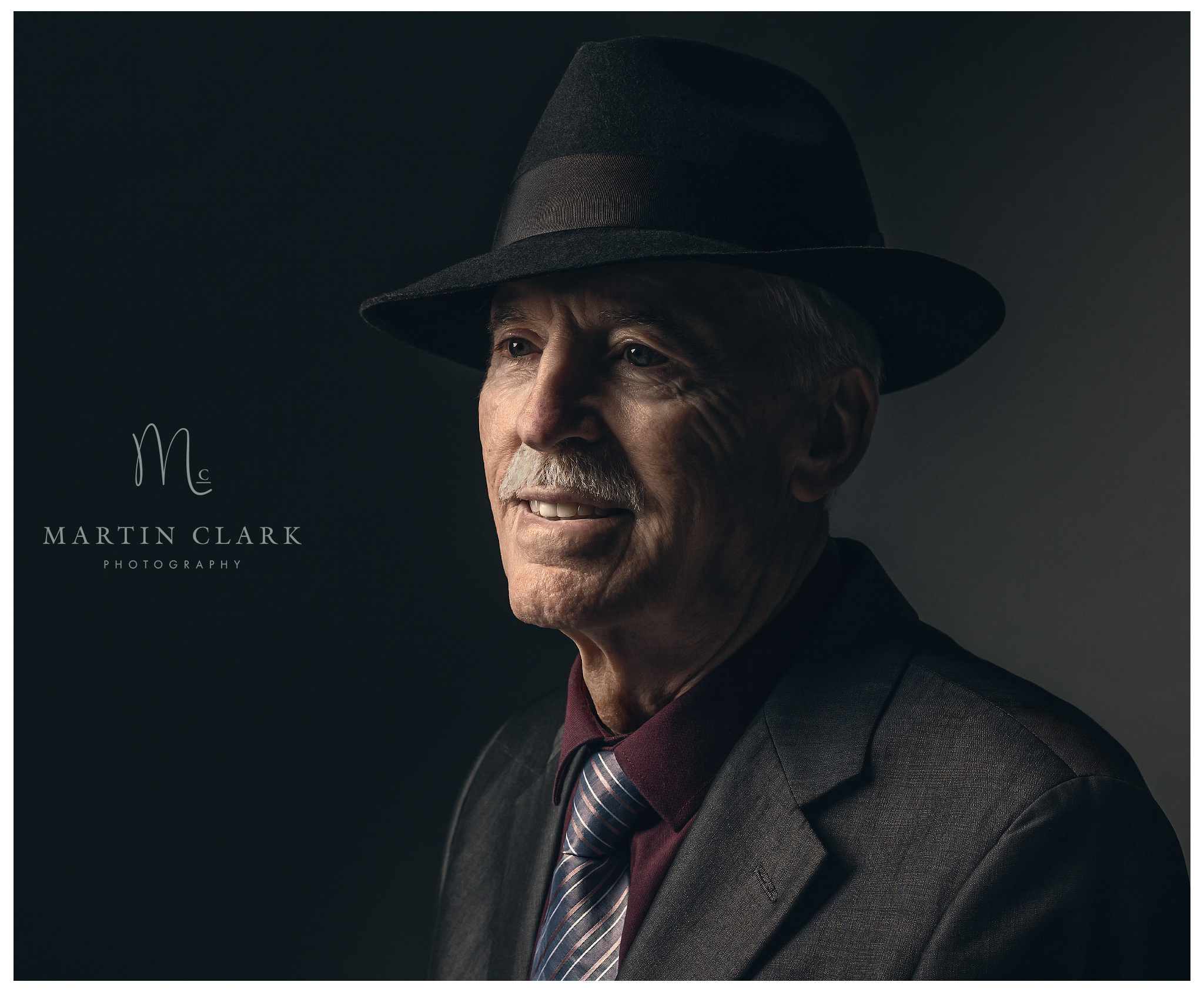 Portrait photograph of an elderly gentleman wearing a suit and tie and black fedora hat