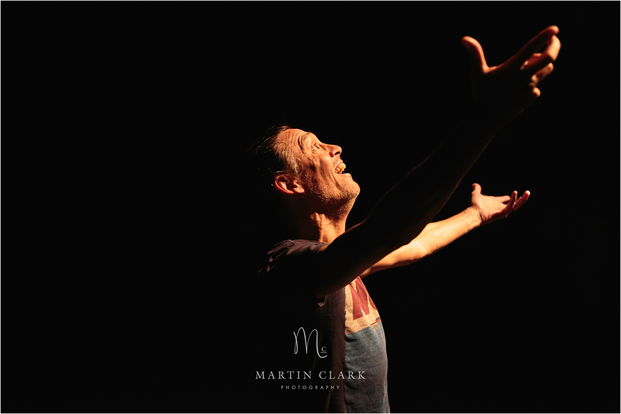 profile view of performer with dramatically outstretched arms in an emotional stage performance