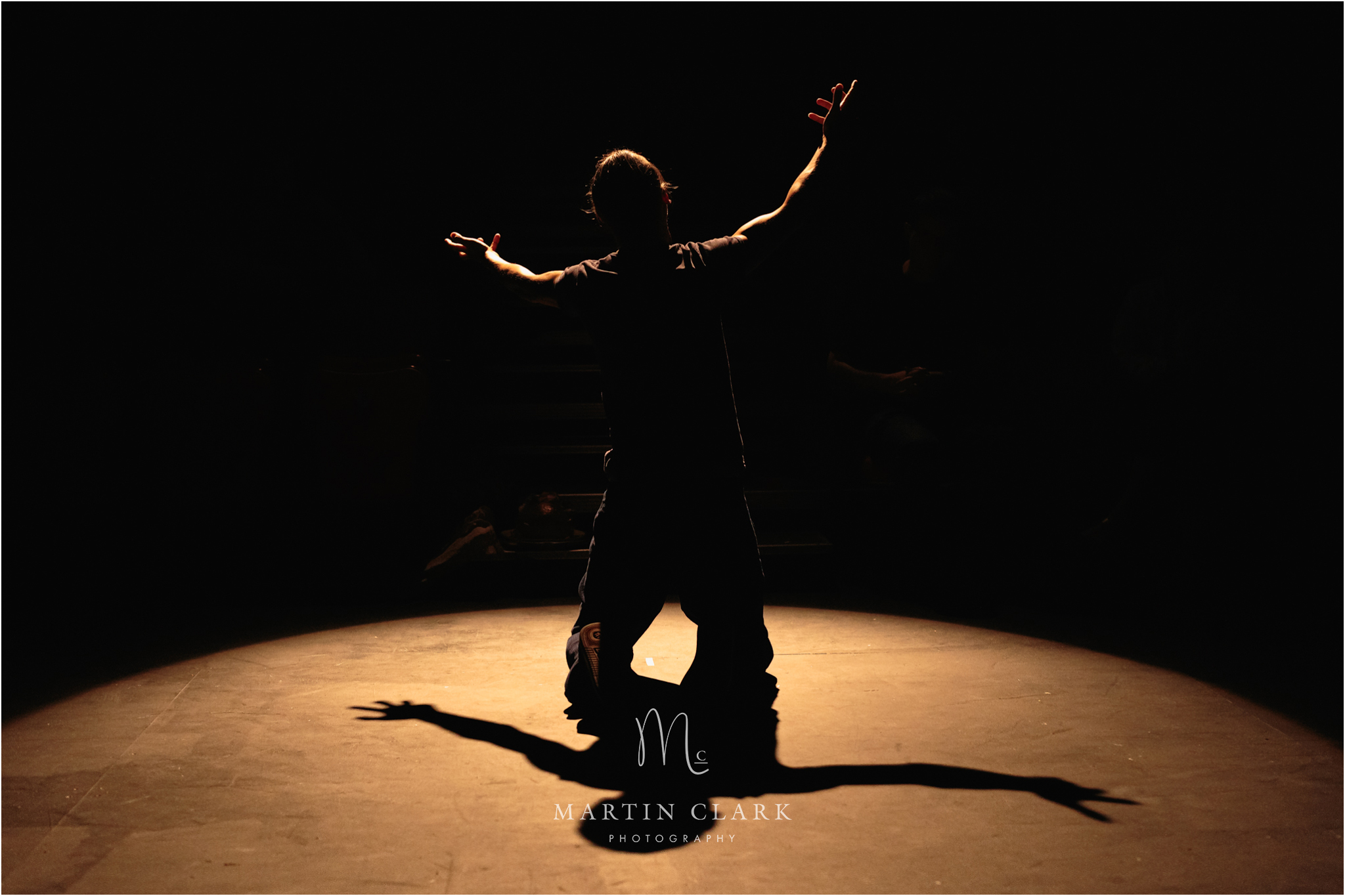 Royal Conservatoire of Scotland performer backlit in stage spot light kneeling with hands outstretched in a dramatic scene