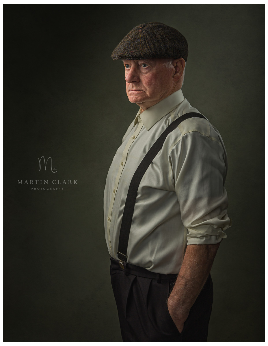 PORTRAIT OF SENIOR MAN STANDING AND WEARING SHIRT AND BRACES AND FLAT CAP