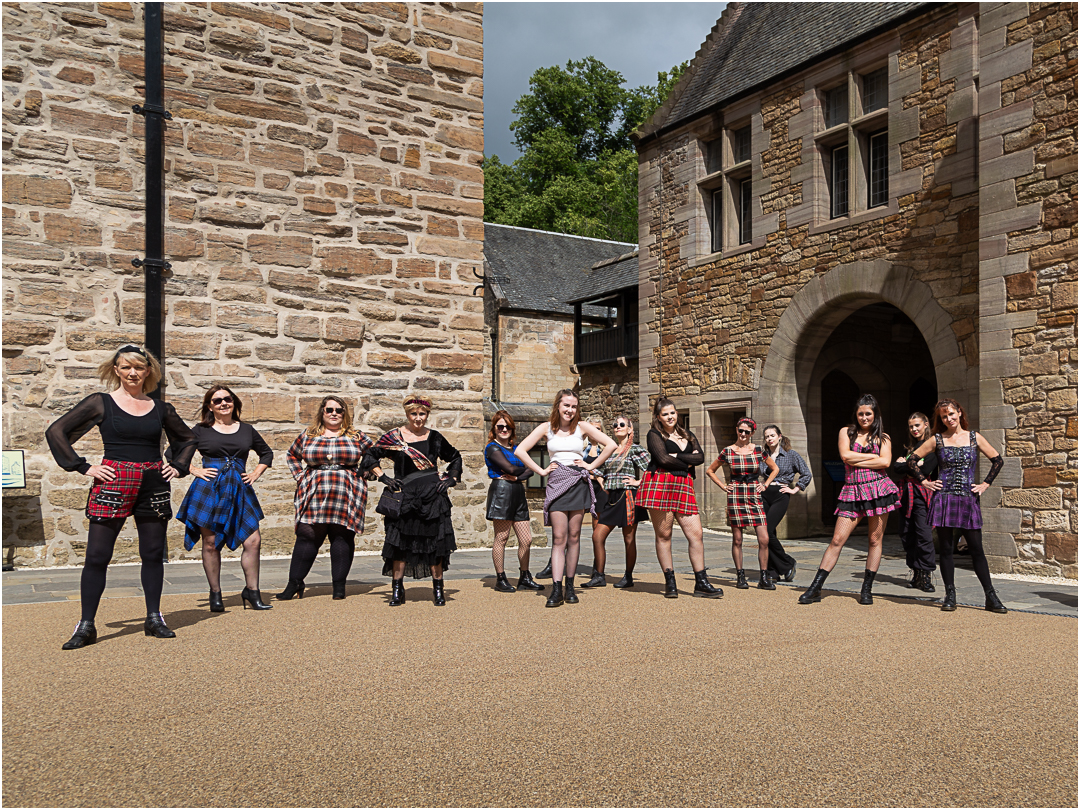 A group of Scottish women dressed in tartan standing in a castle courtyard