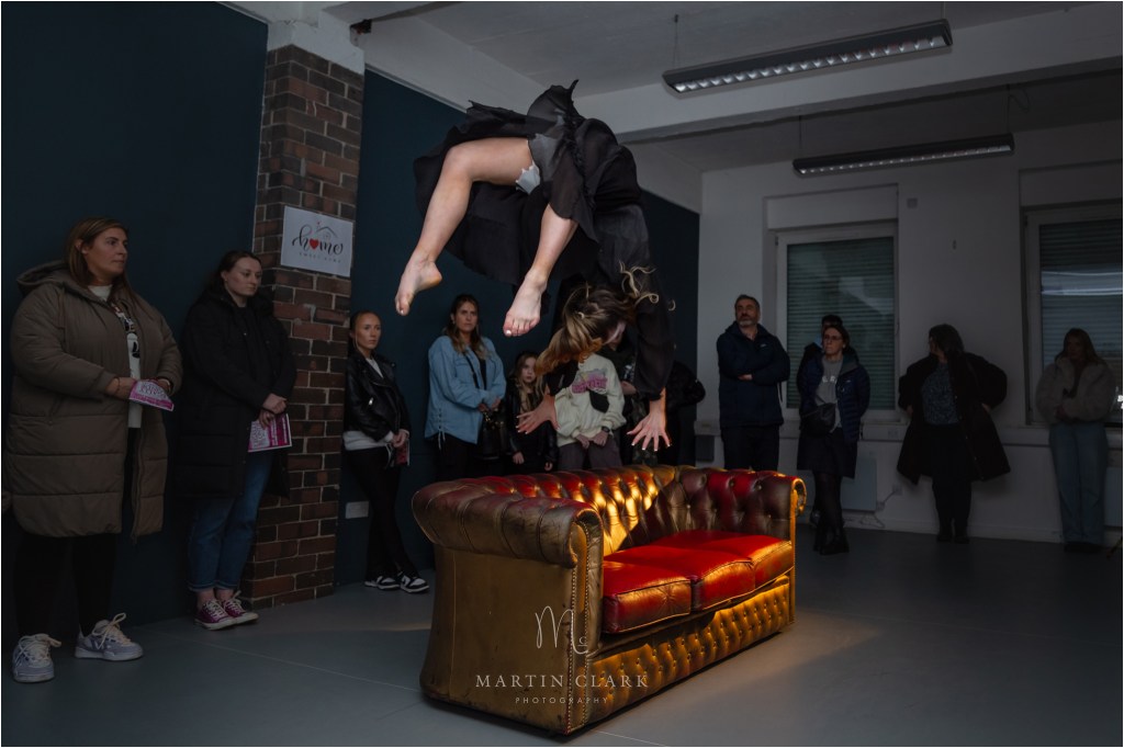 Dramatic dancer performing a backflip over a chesterfield sofa
