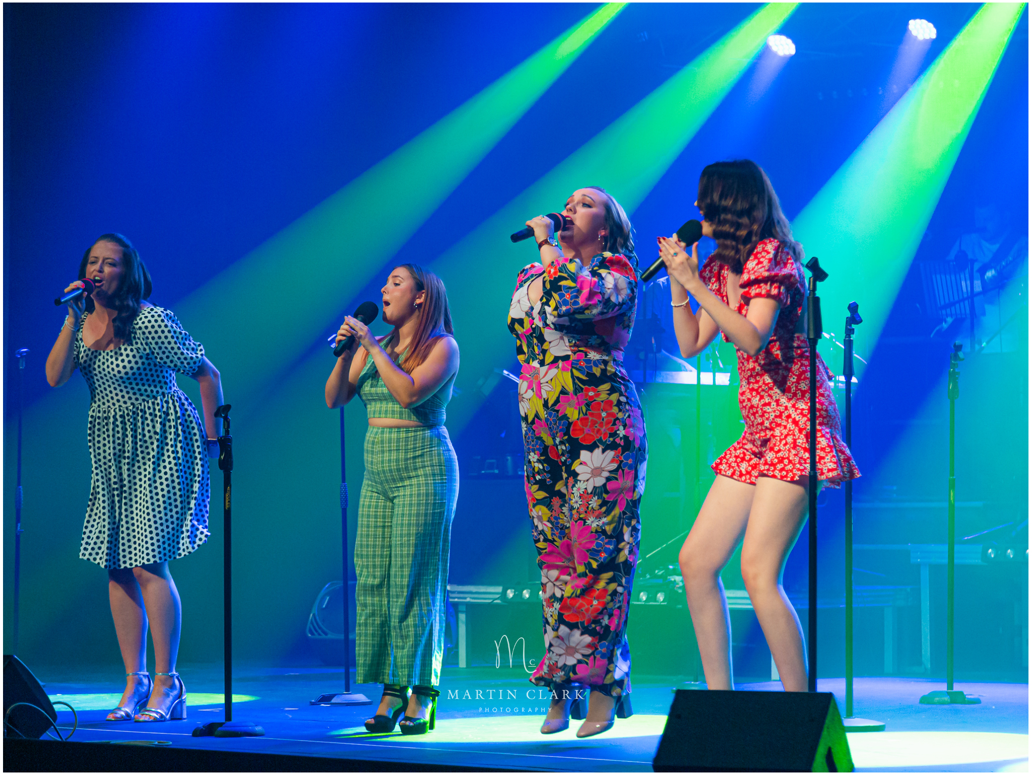 Brightly coloured singers performing on stage with beams of spotlights