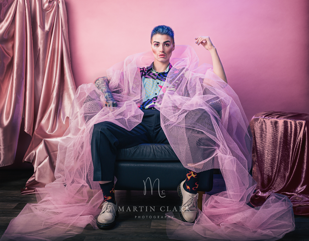 Portrait of transgender model sitting on a chair surrounded by pink material