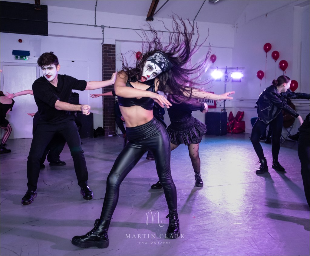 Dancer with long hair shaking head and dressed in leather with clown face makeup
