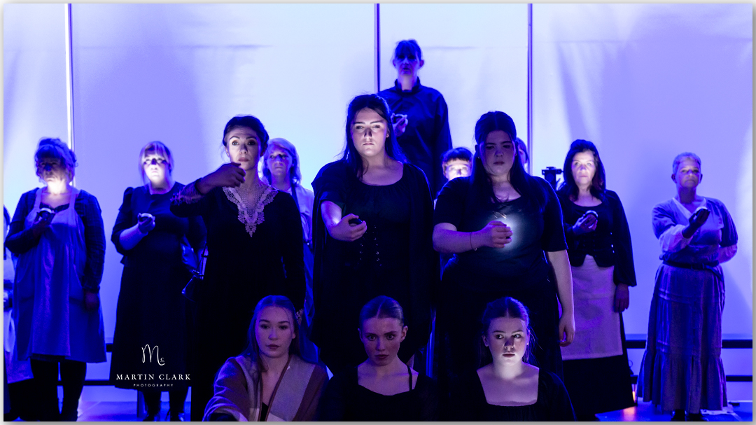 cast performing on stage with torches shining on their faces